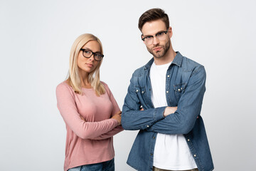 Young couple in eyeglasses looking at camera while standing with crossed arms isolated on grey