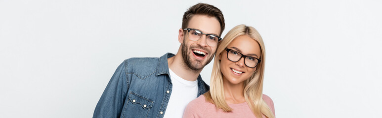 Young couple in eyeglasses smiling at camera isolated on grey, banner