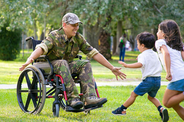 Cheerful kids meeting military dad and running to disabled man in camouflage with open arms for hug. Veteran of war or returning home concept