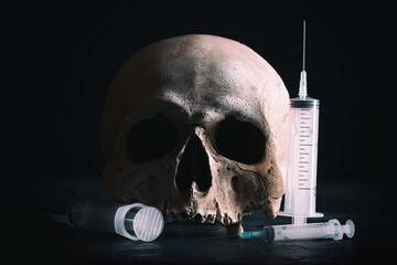Crime and drugs concept. Human skull with syringes on dark background.