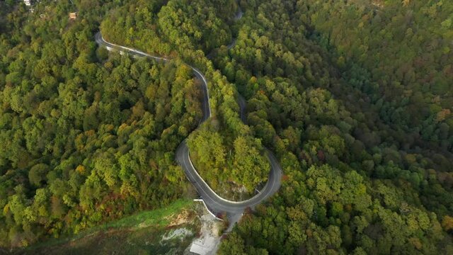 AERIAL. shot of a switchback road winding up a forest covered hill. Flying over a lush green hill with a winding road winding across the hilltop. 