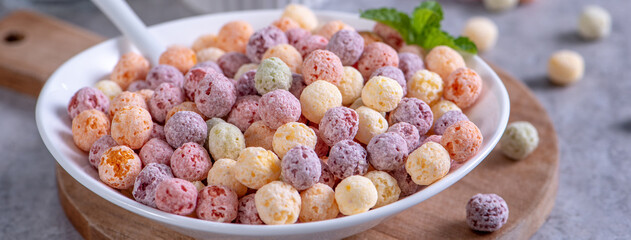 Colorful cereal corn balls mix sweets in a bowl on gray cement background.