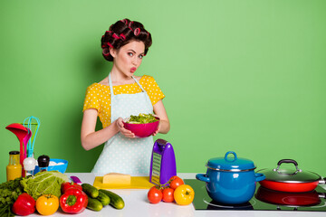 Photo of charming girl hold salad bowl prepare tasty veggie fresh organic dish dinner send air kiss wear yellow dotted t-shirt hair rollers isolated over green color background