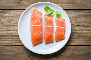 Raw salmon filet with herbs and spices on white plate and wooden background