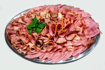 Types of ham and bacon slices on silver plate on white background.