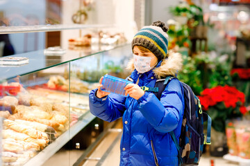 Kid boy wearing medical mask buy bread and pastry for school lunch in bakery. Child with backpack...