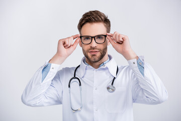 Portrait of confident ophthalmologist holding eyeglasses frame, while looking at camera isolated on white