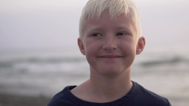 Close-up boy blond smiles against the backdrop of the washed-out sea at sunset. A child on vacation in Sochi.