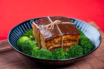 Dong Po Pork meat in a blue plate with broccoli with red background.