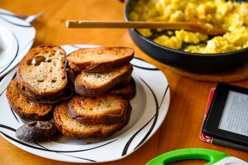 Table with fried toasts, scrambled egg and electronic reader, breakfast.