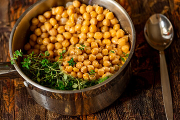 Chickpeas with herb in pot, spoon on dark table.