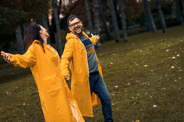 Mid adult couple in raincoat enjoying together and having fun in city park after rain.