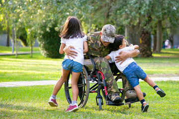 Happy disabled military man in wheelchair returning home and hugging kids. Veteran of war or family...