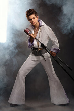 A teenage guy in the image of Elvis Presley with a microphone and a concert costume