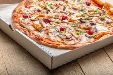 Delicious italian pizza with cheese mozzarella , tomatoes, bacon, mushrooms and green onion in the box on wooden table. Close up view.