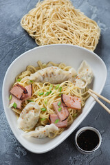 Dry wonton noodles or egg noodles served with wontons and sliced chinese char siu, vertical shot on a grey concrete background