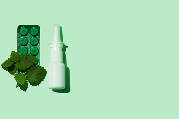 White nasal spray bottle green and tablets plate on aqua mint background flat lay with harsh shadow. Remedy against allergies runny nose, cold flu, viral diseases. COVID-19 pandemic, rhinitis therapy.