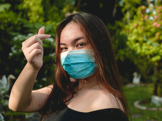A young Filipina girl wearing a face mask makes the heart sign with her thumb and index finger