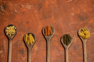 Various mix of dry pasta on wooden spoons.