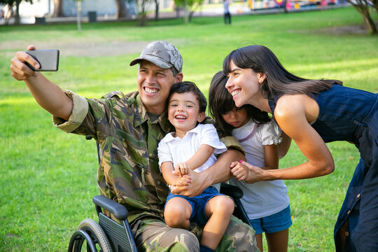 Happy disabled military man taking selfie with his wife and two kids in park. Veteran of war or leisure time with family concept