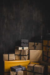Many presents and gifts wrapped in golden paper piled up near black wall.