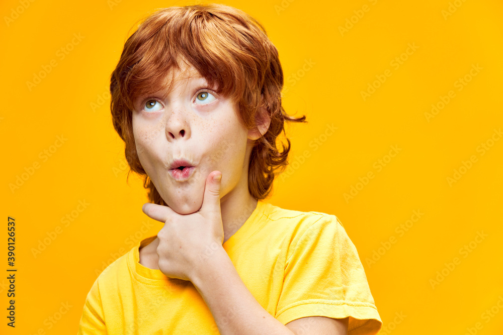 Wall mural surprised red-haired boy looking up hand near chin 