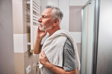 Focused elderly man with a towel looking in bathroom mirror