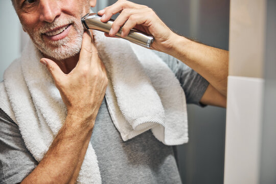 Senior man smiling while shaving his beard with electric device