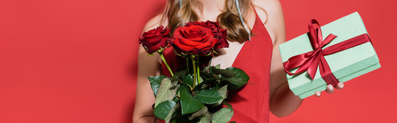 Fototapeta na wymiar cropped view of woman holding roses and gift box on red, banner