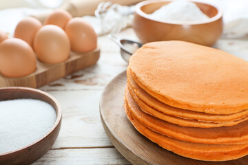 Tasty pumpkin pancakes with ingredients on table