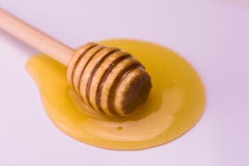 Wooden stick for honey lies in a drop of honey on a white background.