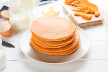 Tasty pumpkin pancakes with ingredients on table