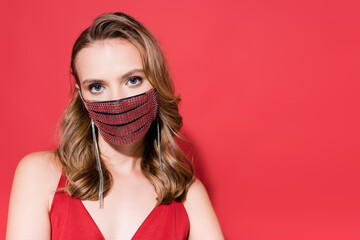 young woman in protective mask with rhinestones looking at camera on red