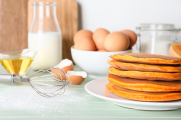 Tasty pumpkin pancakes with ingredients on table