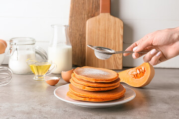 Woman sprinkling sugar powder onto tasty pumpkin pancakes on plate