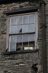 An old, broken sixteen pane Georgian window in a cracked stone wall with rotten wood work.