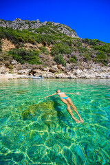 Girl with sun hat relaxing and swimming at Porto Timoni beach at Afionas is a paradise double beach with crystal clear azure water in Corfu, Ionian island, Greece, Europe