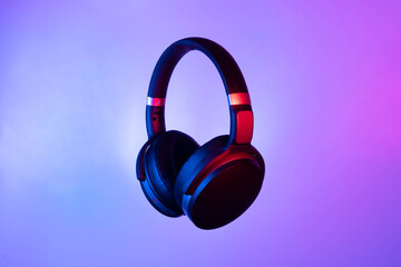 Black wireless bluetooth headphones on neon light background. Music concept.