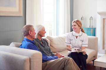 Female Doctor With Mask Makes Home Visit To Senior Couple For Medical Check During Covid-19 Lockdown