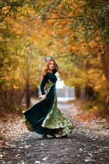 Queen with red hair in a green dress with a crown in the forest