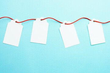 Row of blank gift tags mock-ups on red ribbon string on blue background. Discount or sale concept. 