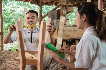 man carpenter measuring wood using ribbon ruler and business woman using tablet pc at the workshop