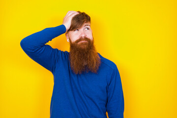 Young handsome red haired bearded man standing against yellow wall saying: Oops, what did I do? Holding hand on head with frightened and regret expression.