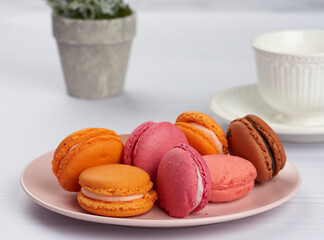 baked macarons on a pink plate, behind a ceramic white cup with coffee