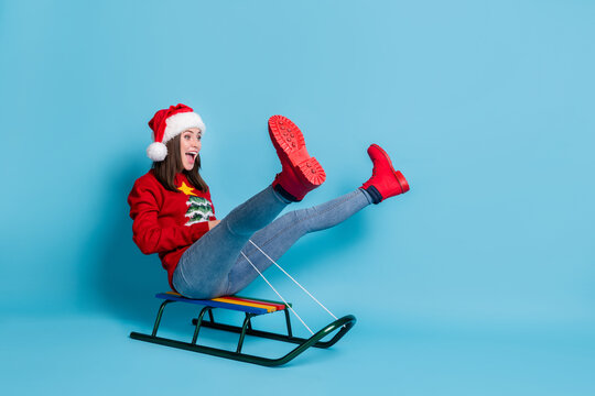 Photo portrait of young woman riding sled with legs up isolated on pastel light blue colored background
