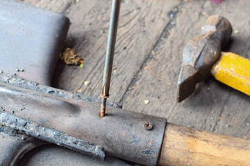 Screwing rusty screw into an old shovel with screwdriver