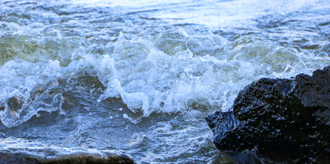 waves run onto the shore and crash against the rocks, creating many splashes and splashes near the shore. river surf in stormy weather near a stone pebble coast with foamy splashing waves.