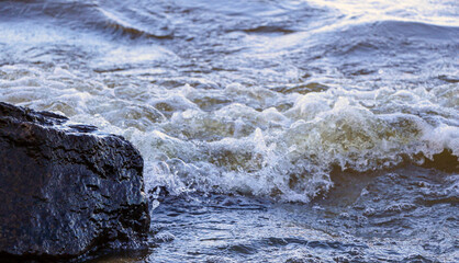 waves run onto the shore and crash against the rocks, creating many splashes and splashes near the shore. river surf in stormy weather near a stone pebble coast with foamy splashing waves.