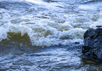 waves run onto the shore and crash against the rocks, creating many splashes and splashes near the shore. river surf in stormy weather near a stone pebble coast with foamy splashing waves.