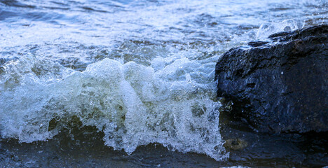 waves run onto the shore and crash against the rocks, creating many splashes and splashes near the shore. river surf in stormy weather near a stone pebble coast with foamy splashing waves.